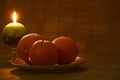 ÃÂ¡hristmas and New Year composition: oranges on ceramic plate and burning Christmas candle on dark background. Close-up.